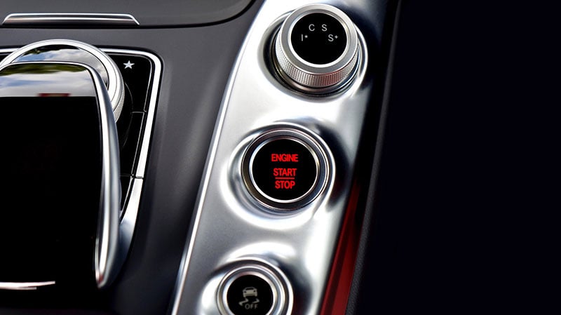 A close up of a car operation panel with a button lighted up with the text: "ENGINE START|STOP"