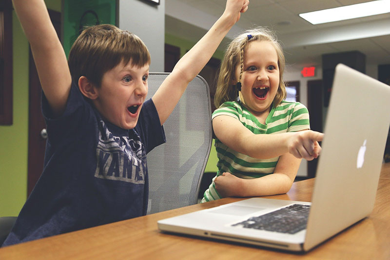2 kids being excited about the content they see on the screen of a macbook