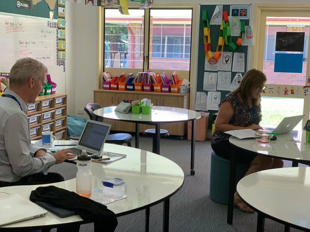 Two teacher sitting on 2 different tables to deliver online lessons